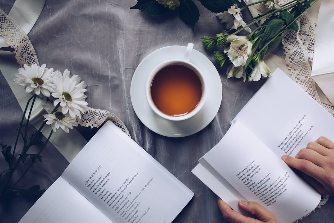 Free Inviting cozy reading setup with tea, poetry books, and fresh flowers on a table. Stock Photo