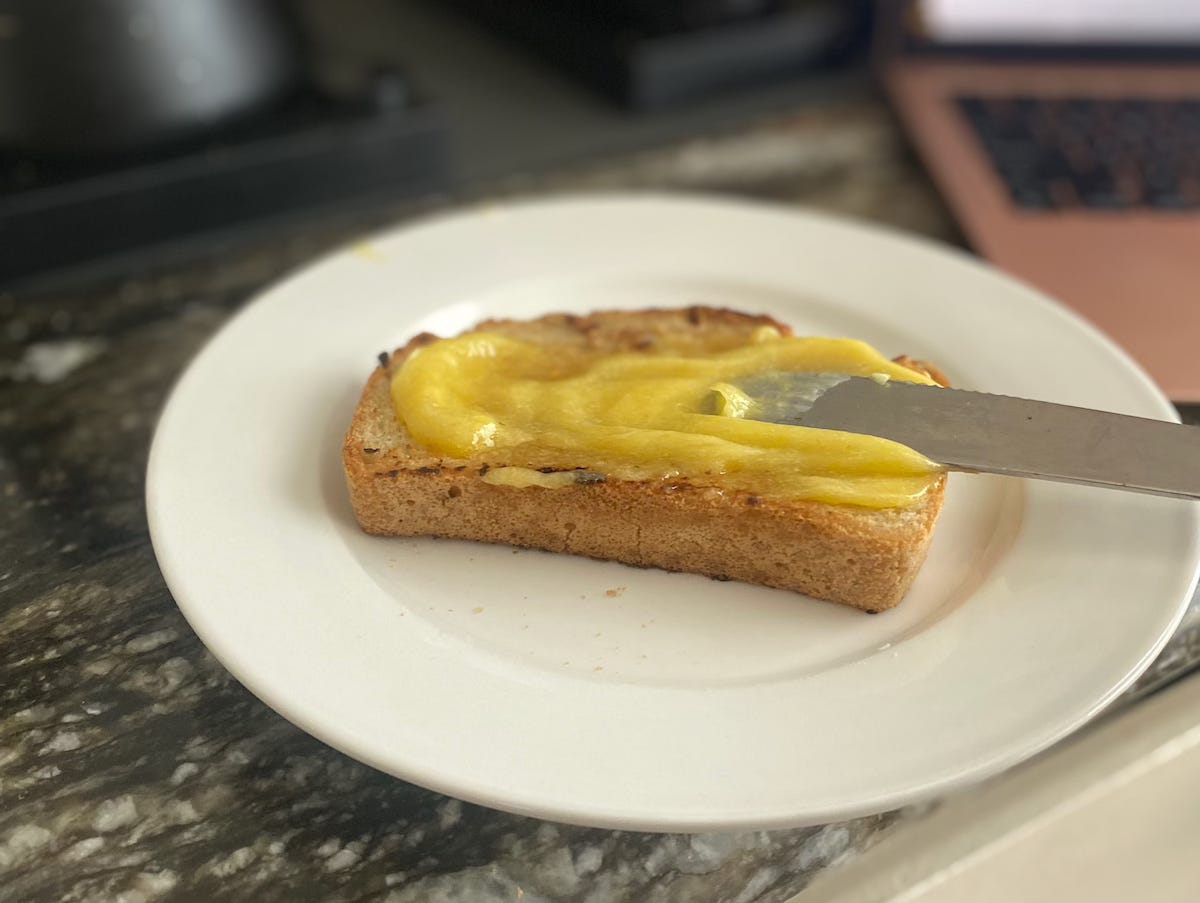 a piece of buttered toast with a knife spreading lemon curd on top