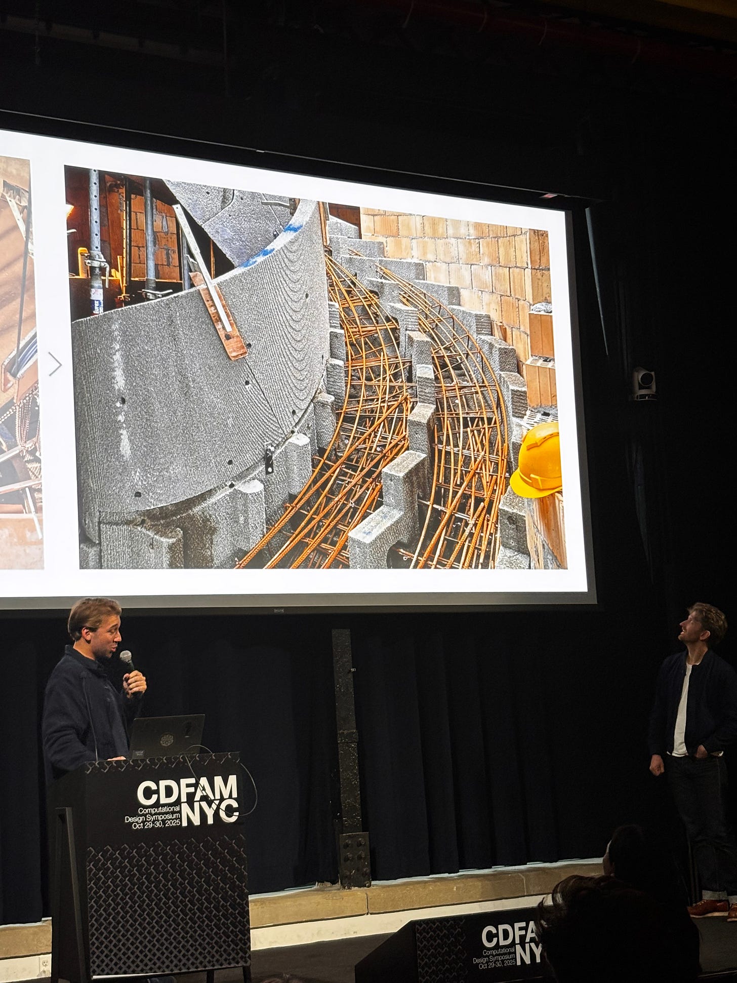 A construction site image featuring workers discussing a curved concrete structure, with exposed reinforcement bars and visible blocks forming the base.