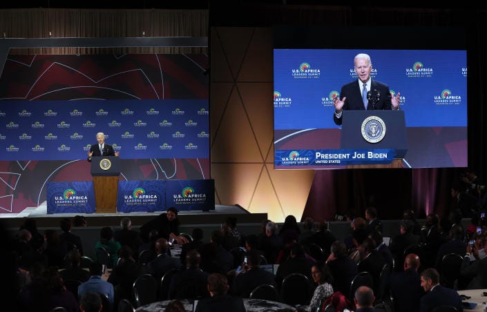 President Biden is seen speaking on stage and on a large screen.