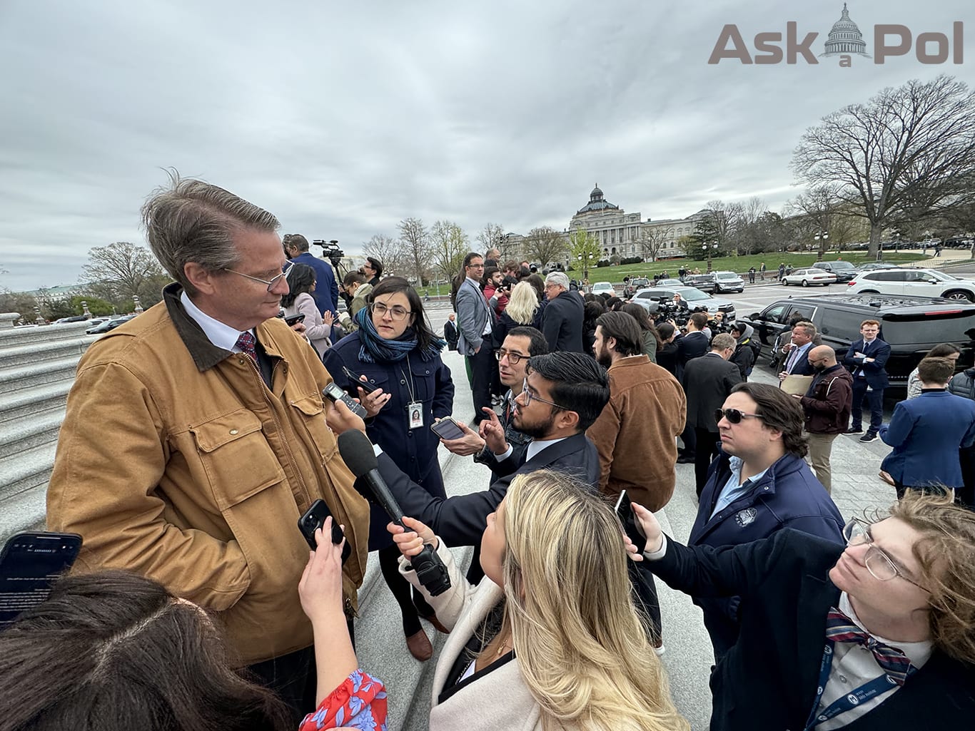 Man in red tie and light brown work jacket takes questions from reporters on US Capitol steps. Photo: Matt Laslo for © www.askapol.com 