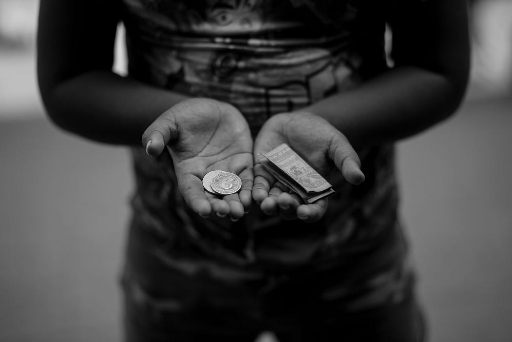 A young person with open palsm holding coins and a few dollars - Photo by Md Arif Hasan on Unsplash