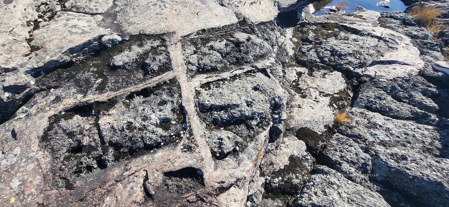 A close-up photograph of rough, textured bedrock at Neys Provincial Park. Large, sharp, angular chunks of darker rock are embedded chaotically within a finer-grained, lighter-colored rock matrix, looking like broken puzzle pieces frozen in place