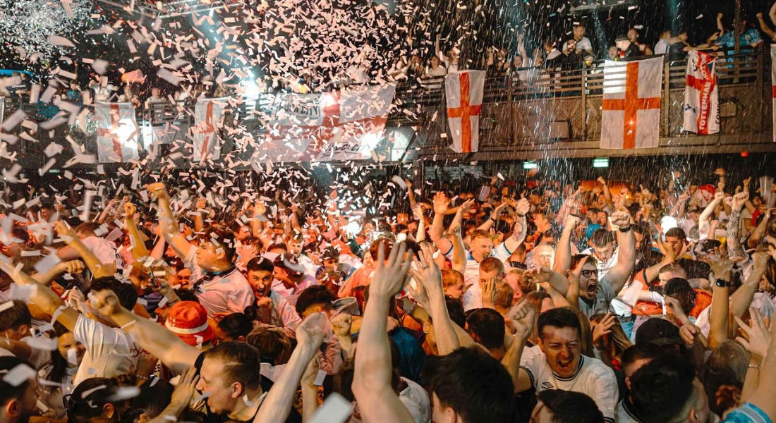 A concert hall with crowds of people, white confetti, and England flags A concert hall with crowds of people, white confetti, and England flags