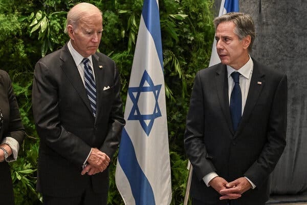 President Biden and Secretary of State Antony J. Blinken stand next to each other with their hands folded in front of Israeli flags.