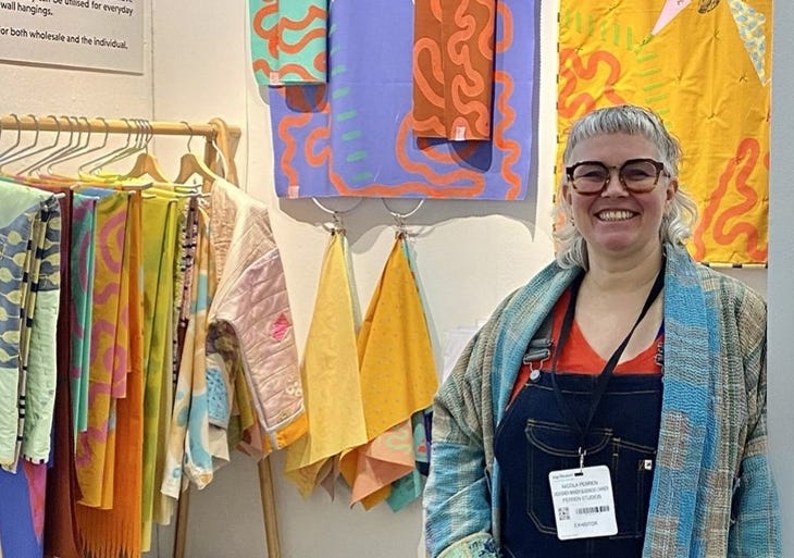 A woman posing alongside some colourful textile artworks A woman posing alongside some colourful textile artworks