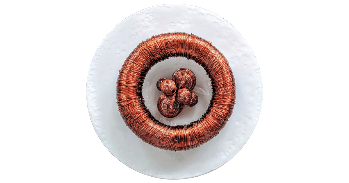 Top down view of an abstract sculpture titled Cinis Incubator 1 by Michal Plis, featuring a large circular ring tightly wrapped in reflective copper wire, surrounding a central cluster of small, coiled copper cones on a textured white circular base.