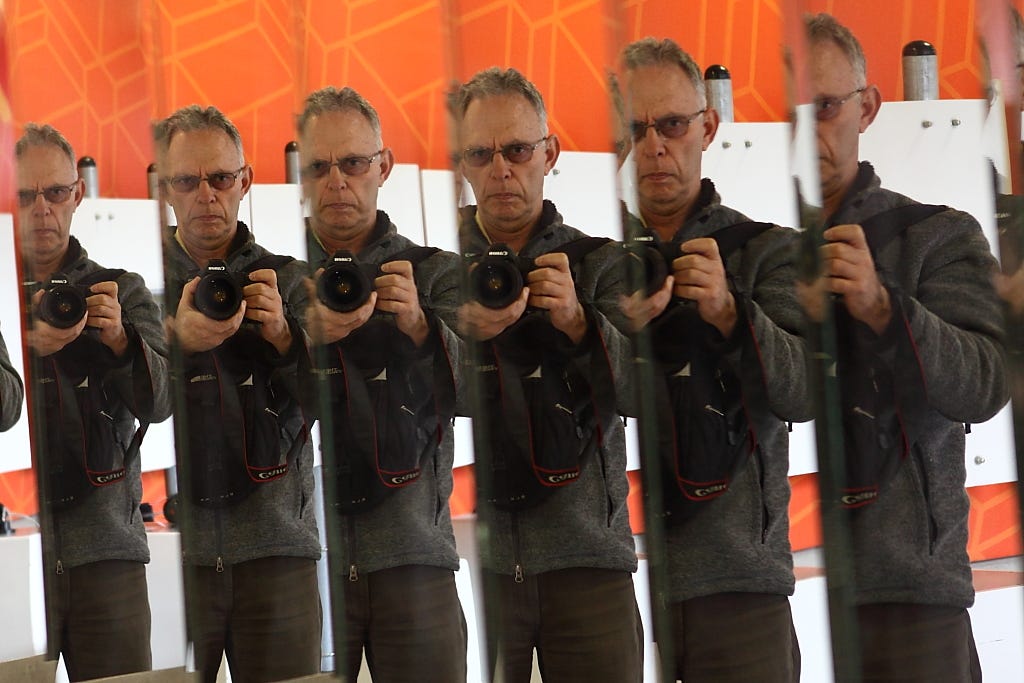 A man holding up a camera. He is reflected multiple times in a mirror.