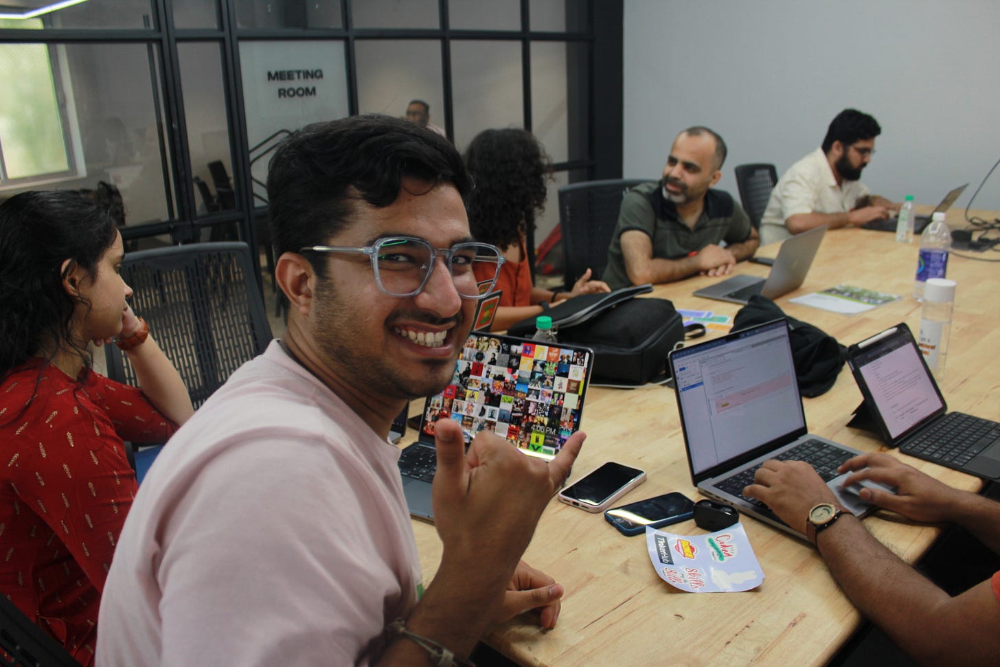 A person in glasses sitting at a table with a laptop and looking at the camera with a smile