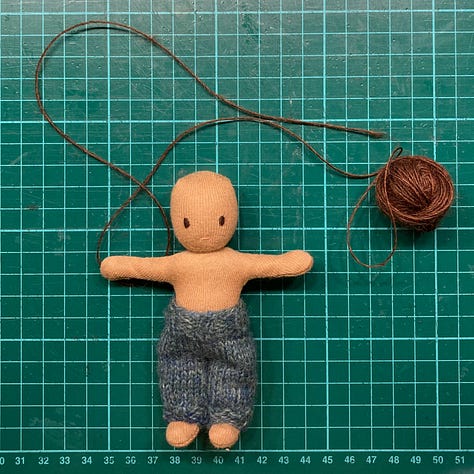 Three photos showing before, during and after the process of sewing brown wool hair onto a small handmade cloth doll made by Illustrator HannahSangjuinetti. The doll has coffee coloured skin and a blue knitted hat and is shown alongside the sketch of an illustration she will eventually be part of.