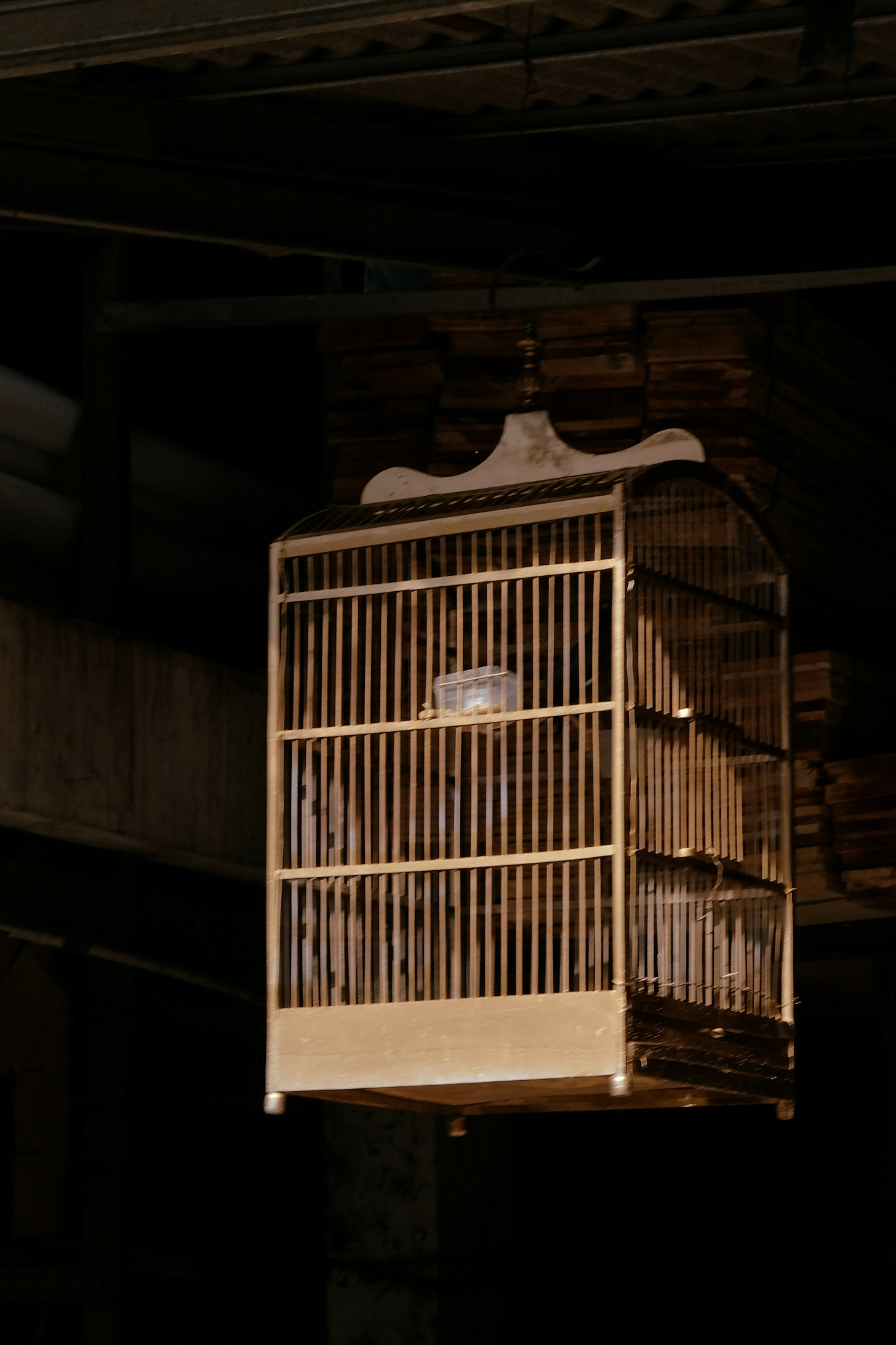 wooden bird cage is seen against a very dark background, the sun illuminates most of the cage wooden bird cage is seen against a very dark background, the sun illuminates most of the cage