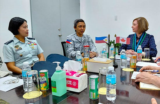 Assistant Deputy Minister (Public Affairs) Geneviève Binet sits at a meeting table with a senior Armed Forces of the Philippines officer as they discuss gender and development initiatives, with Canadian and Philippine flags displayed between them.