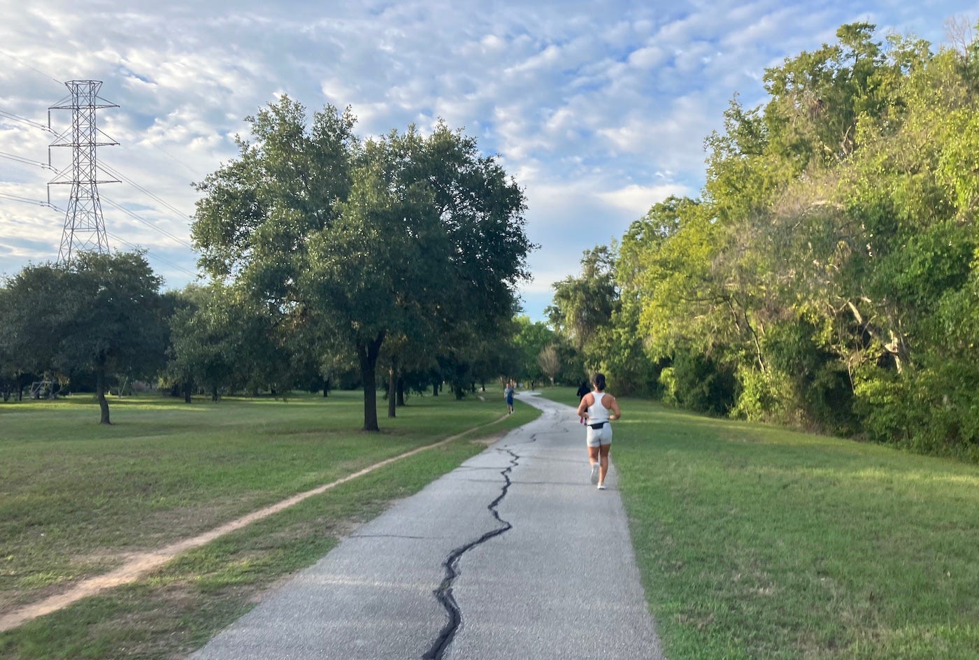 Running along a hard concrete trail past trees and an electricity pylon