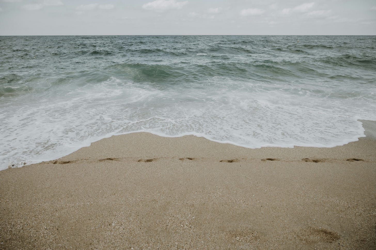 a foggy beach with footsteps in the sand. 