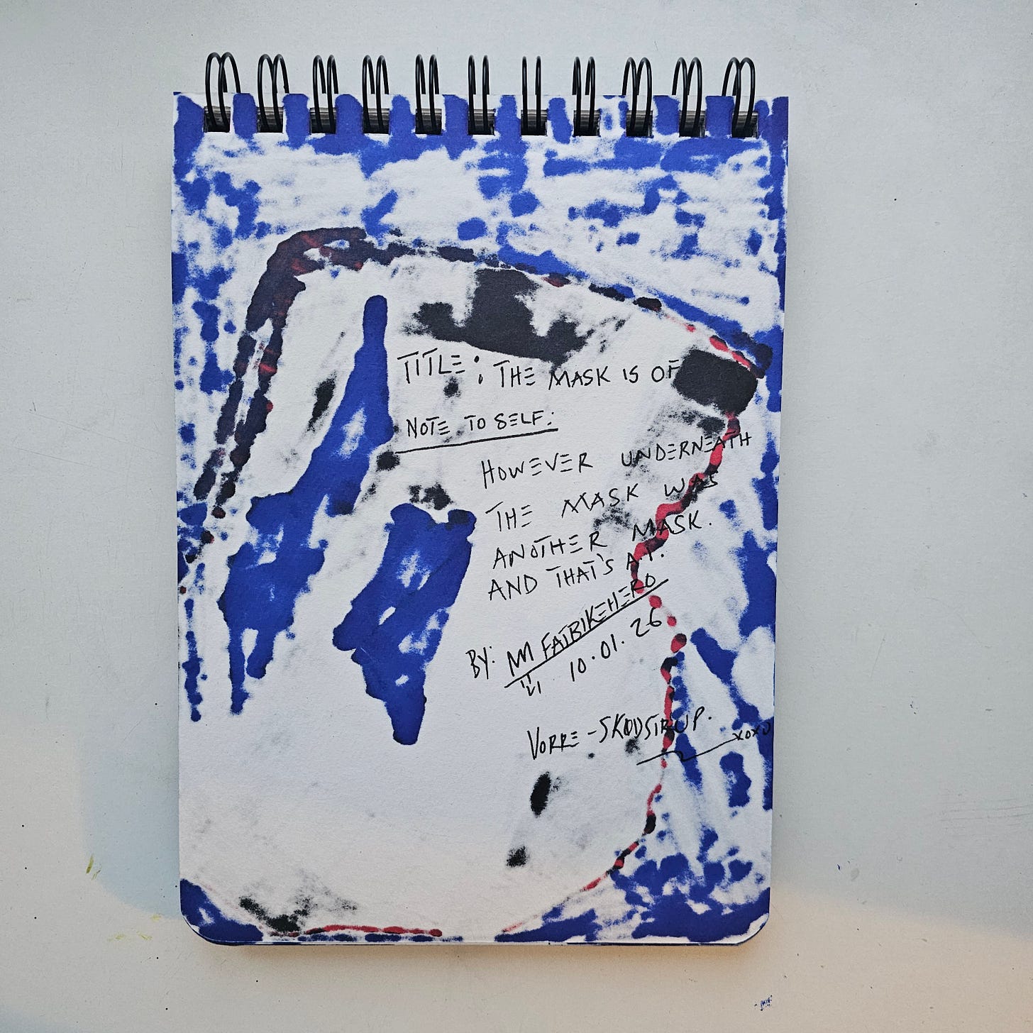 Alt Text: Handwritten sketchbook page by artist FatbikeHero with the text "However underneath the mask was another mask" on a blue and white textured background.