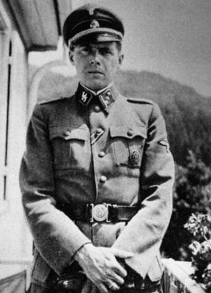 Photograph of Josef Mengele, shown in SS uniform with insignias, standing on a balcony.