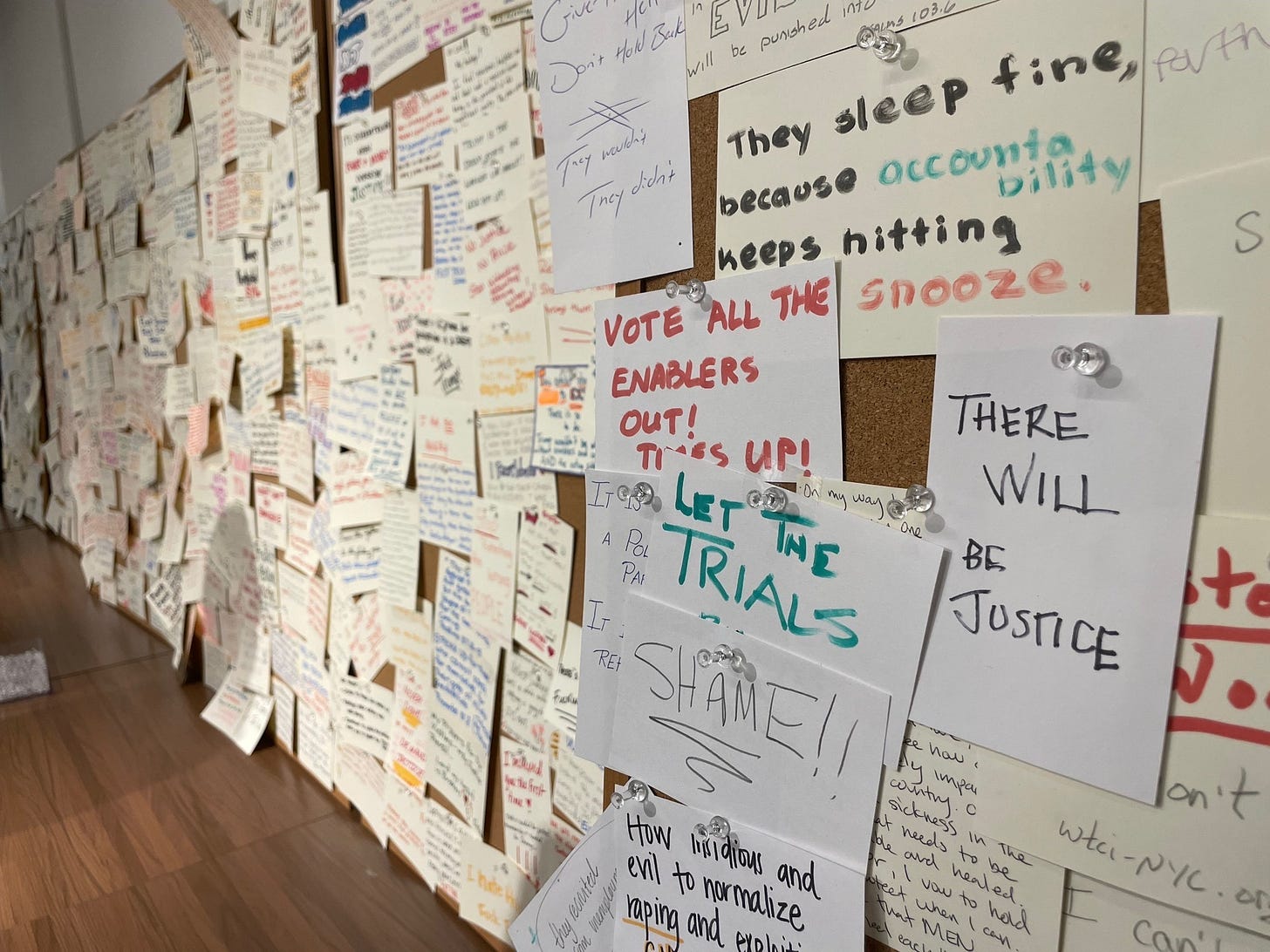 Photo of a wall covered with 3"x5" note cards with handwritten messages, in magic marker, that say things like "There will be justice," "Shame!," and "Vote all the enablers out! Times up!" 