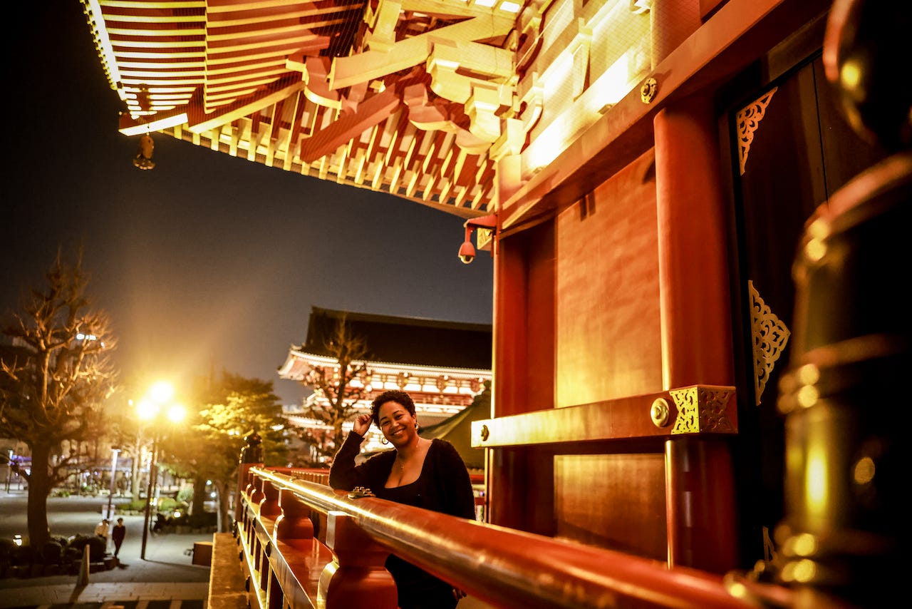 anela stands at night on a balcony in front of a railing at the temple, smiling
