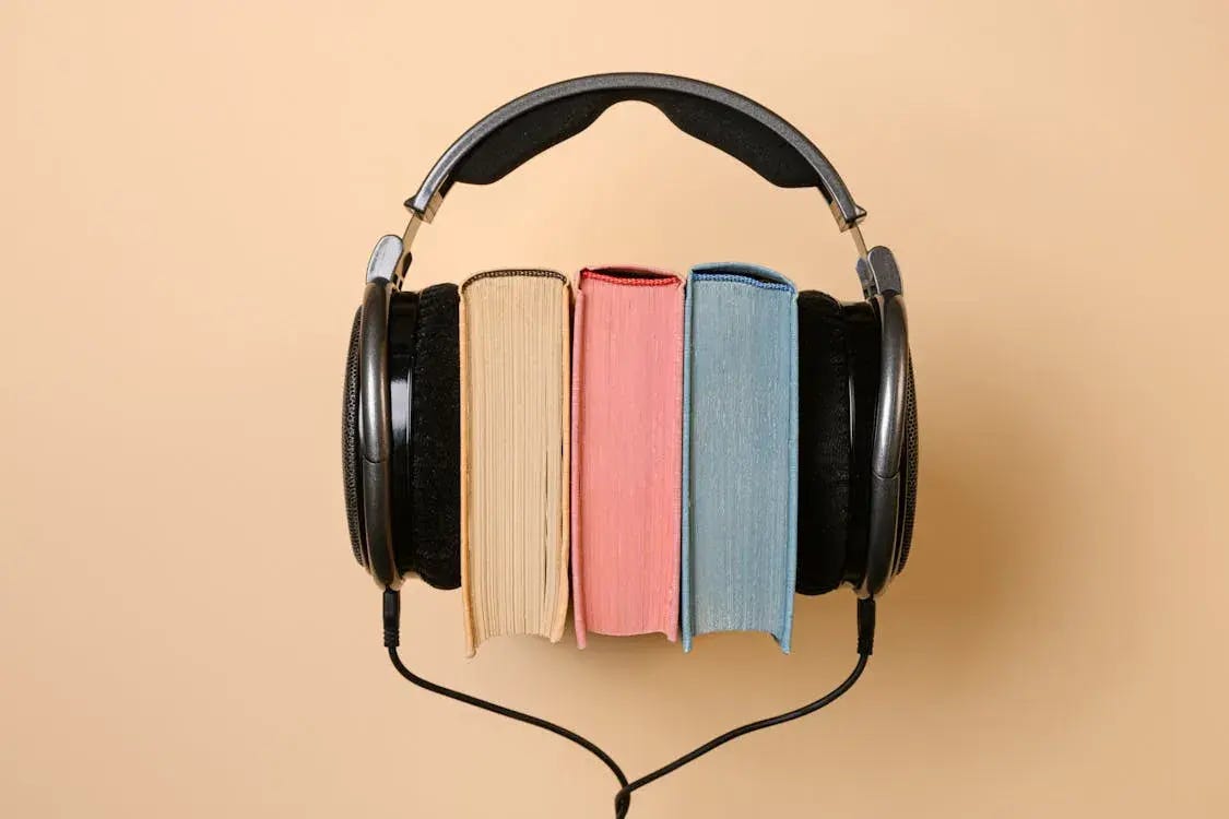 Three books placed between large black headphones against a beige background, symbolizing audiobooks or reading with audio.