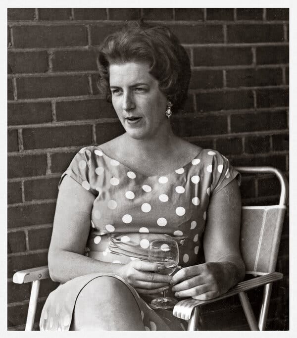 A black and white photo of Yvonne Barr sitting in front of a brick wall and wearing a dress with polka dots. A black and white photo of Yvonne Barr sitting in front of a brick wall and wearing a dress with polka dots.