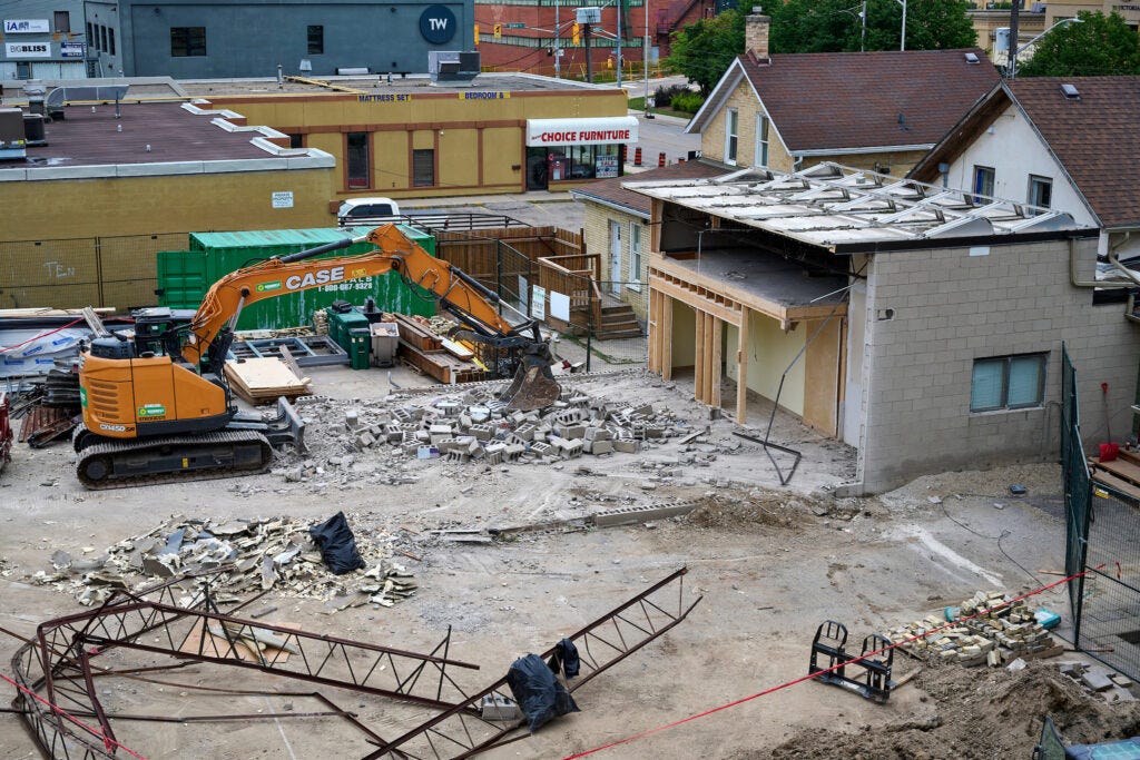 An orange CASE excavator demolishes the garage on Victoria for the Making Home project in Kitchener, Ontario, 2024.