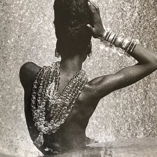 This may contain: a woman standing in the water with her hands on her head and necklaces around her neck