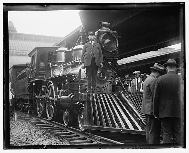 a black and white photo of a man standing on the front of a train a black and white photo of a man standing on the front of a train