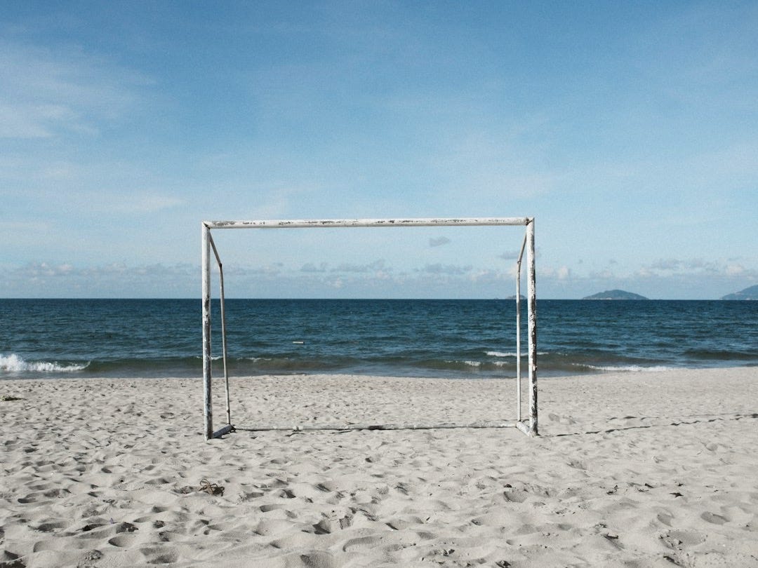 a soccer goal on a beach with the ocean in the background
