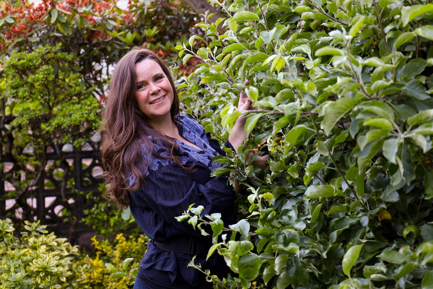Stephanie in garden smiling next to a shrub Stephanie in garden smiling next to a shrub