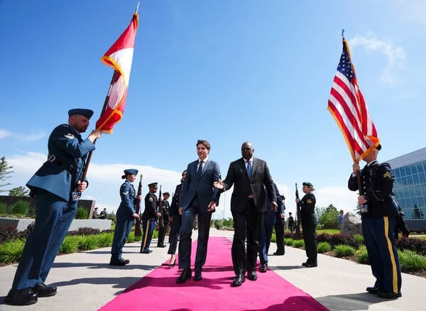 Mr. Trudeau, left, walks down a red carpet outdoors, next to another man, with soldiers on either side.