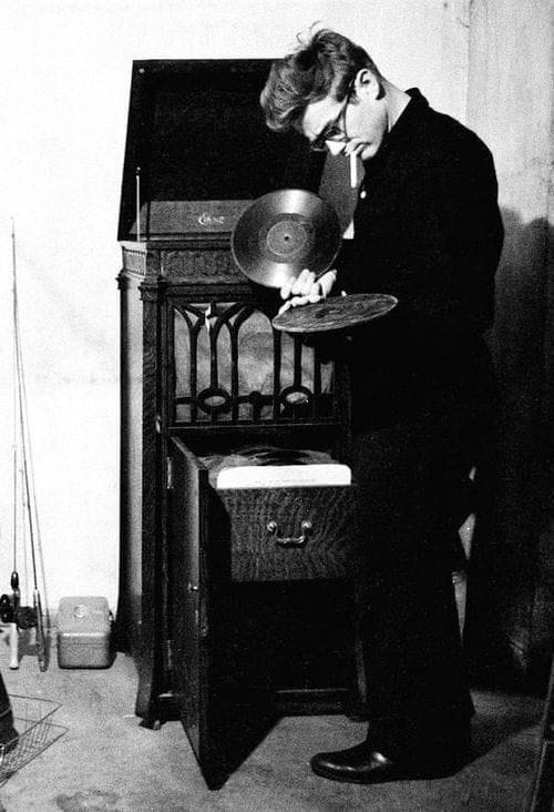 This may contain: black and white photograph of a man holding a pan in front of an old record player This may contain: black and white photograph of a man holding a pan in front of an old record player