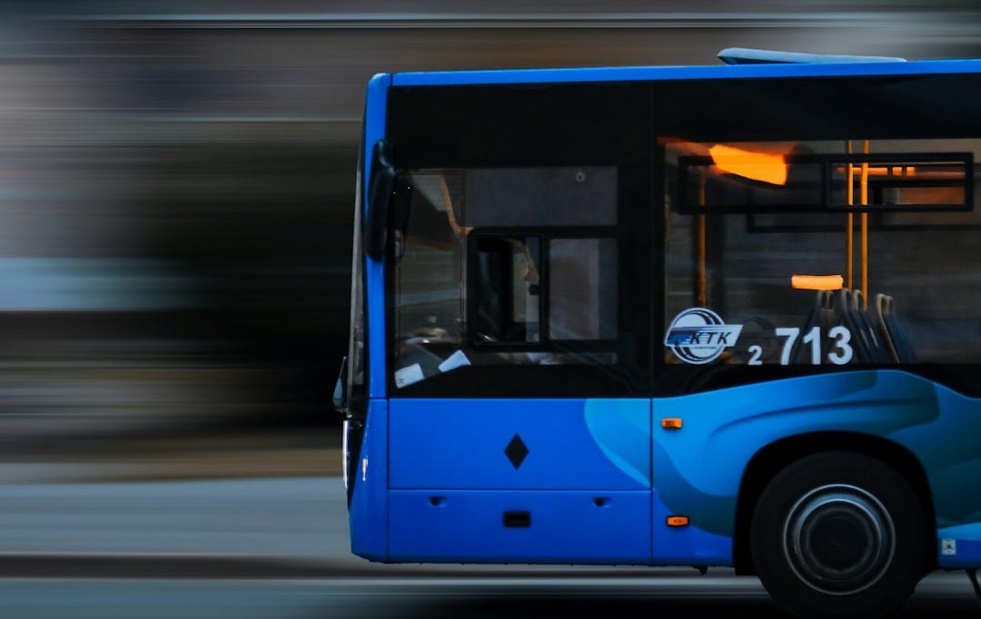 a blue bus driving down a street next to a tall building
