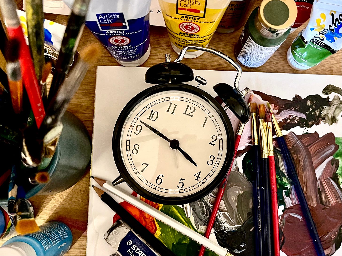 alarm clock lying on a paint palette surrounded by art supplies alarm clock lying on a paint palette surrounded by art supplies