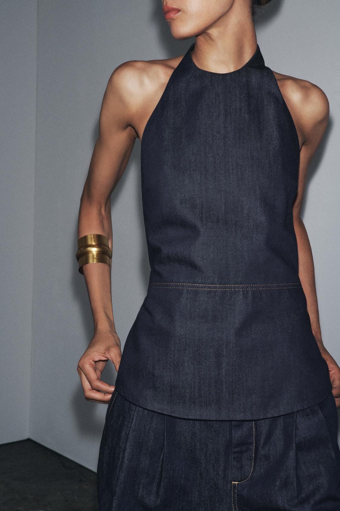 Medium shot of a sleeveless blue halter neck top with pronounced topstitching. Open back.