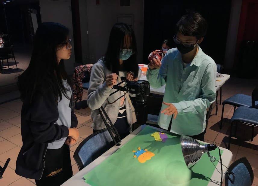 Maria Fong showing two teens how to use the downshooter camera to create stop motion animation with paper puppets
