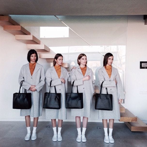 This may contain: four women in grey suits holding black bags and standing next to each other with their hands on their hipss