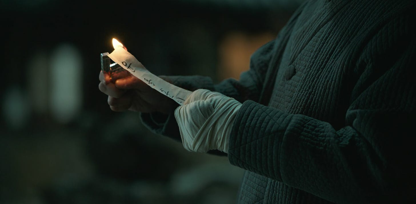 Choi Mu-jin at the temple's front yard, burning a piece of parchment with Yoon Dong-hoon's name on it, episode six of My Name (2021)