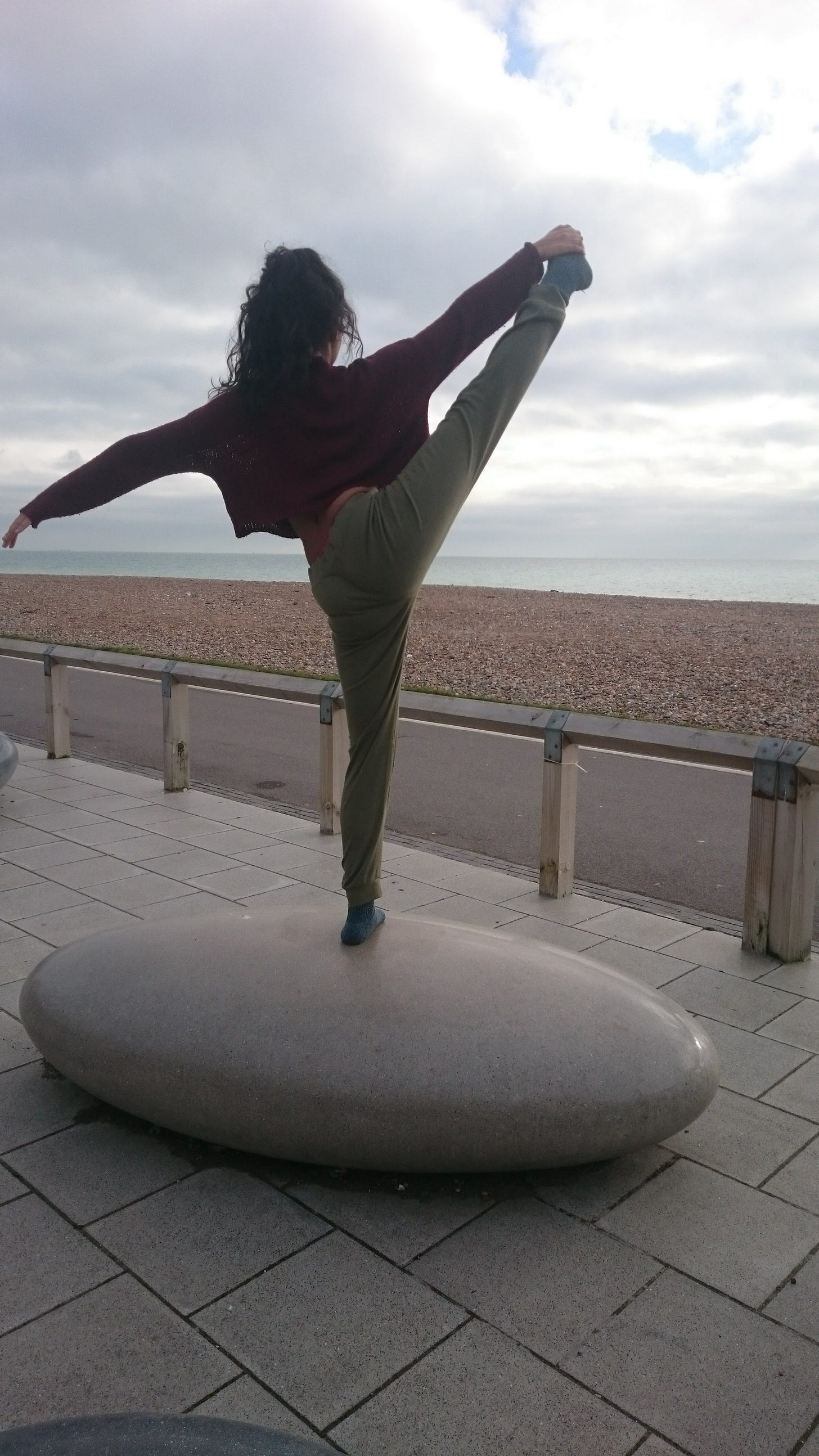 black dancer in leg extension, balanced on a stone, looking out to the sea