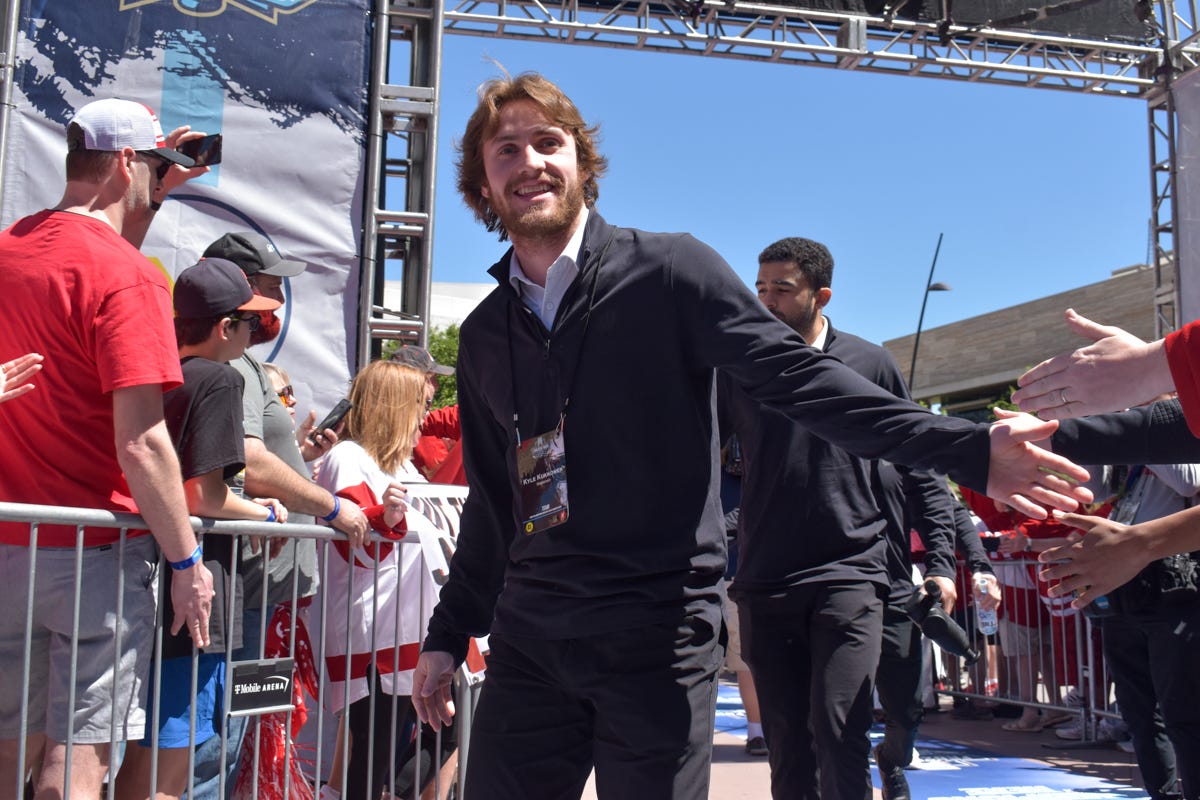 Kyle Kukkonen in black pants and a black Wisconsin branded quarter zip smiles and high-fives fans