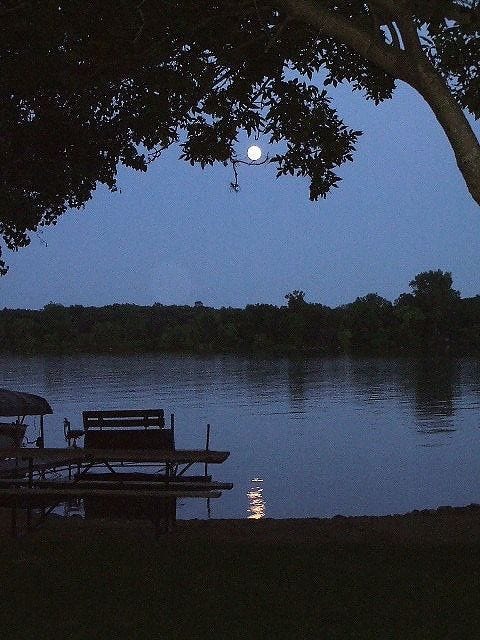 This may contain: the moon is setting over the water at night