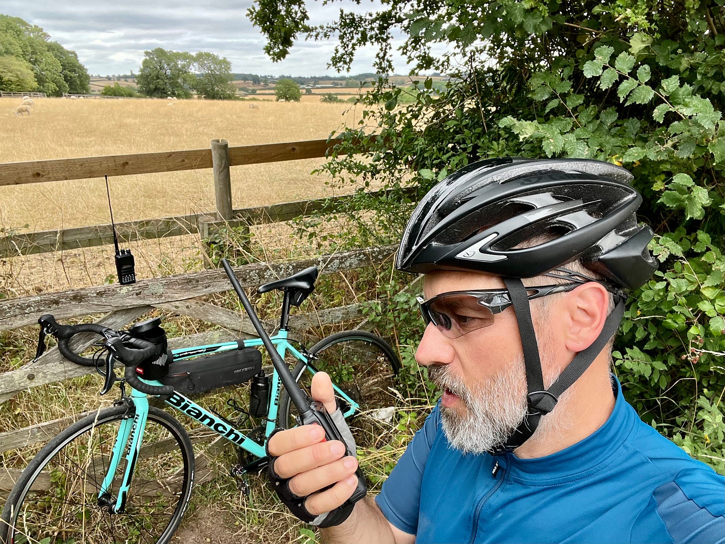 A selfie of me on a borrowed bike with two handheld radios on a hill.