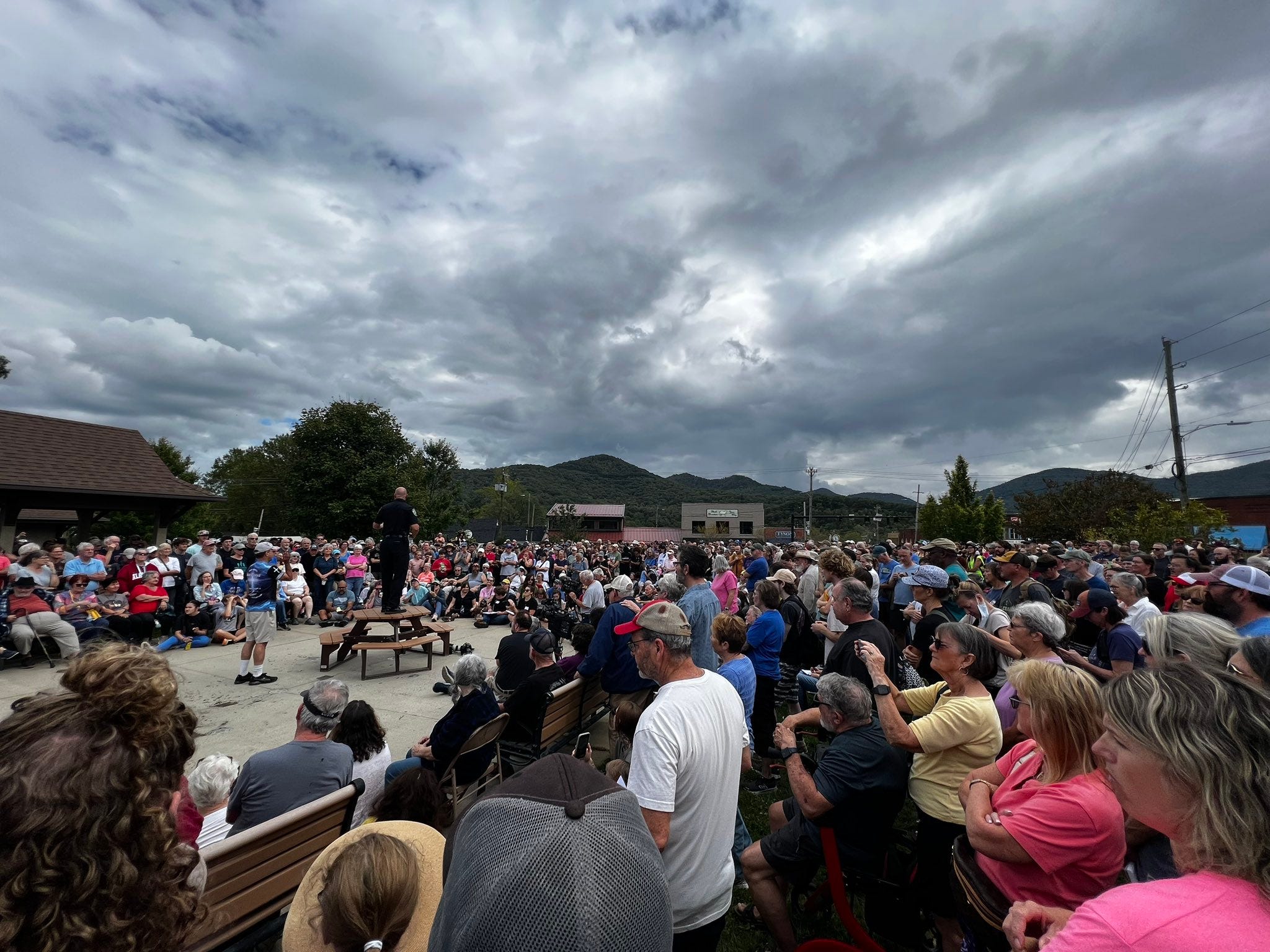 Hundreds of people gathered around a police officer speaking on a picnic table Hundreds of people gathered around a police officer speaking on a picnic table