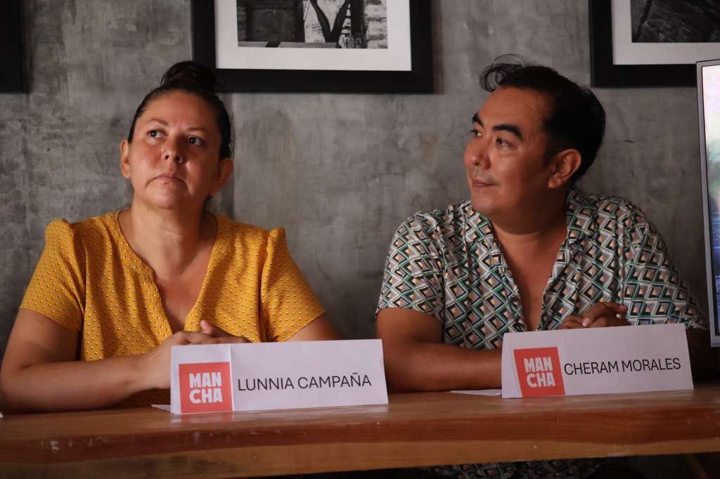 Two MANCHA Festival organizers, Lunnia Campaña and Cheram Morales, sit at a table during a press event, each with a name placard in front of them. Campaña looks upward in thought, while Morales glances toward her, framed by gray walls and black-and-white photos behind them. Two MANCHA Festival organizers, Lunnia Campaña and Cheram Morales, sit at a table during a press event, each with a name placard in front of them. Campaña looks upward in thought, while Morales glances toward her, framed by gray walls and black-and-white photos behind them.