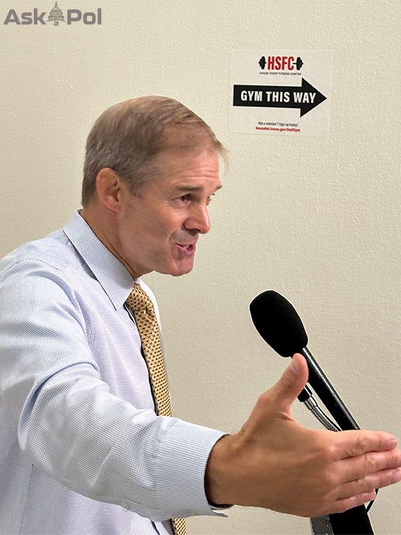 A congressman in a tie without a suit coat on speaks into a mic while waving his hand for emphasis 