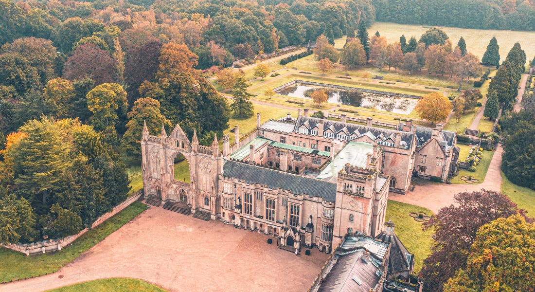 A wide shot of Newstead Abbey with a path in front of it, a garden behind it, and trees around it