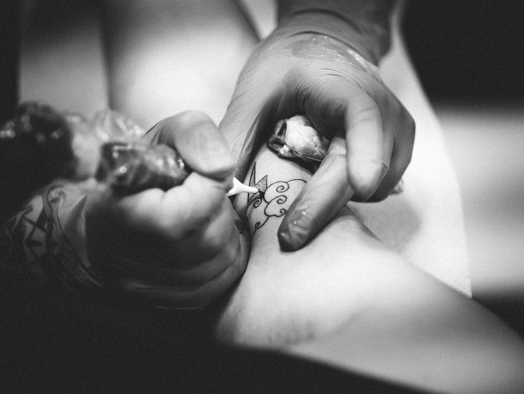 A black and white shot shows a man tattooing.