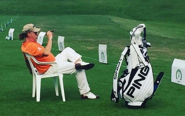 This may contain: a man sitting in a chair on top of a green field next to a golf bag This may contain: a man sitting in a chair on top of a green field next to a golf bag