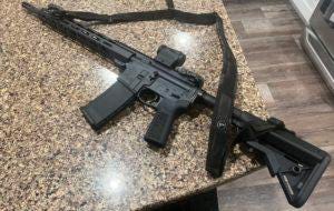 An AR-15 with a common setup, including collapsible stock, folding backup sights, a red dot sight, and a 2 point sling. 