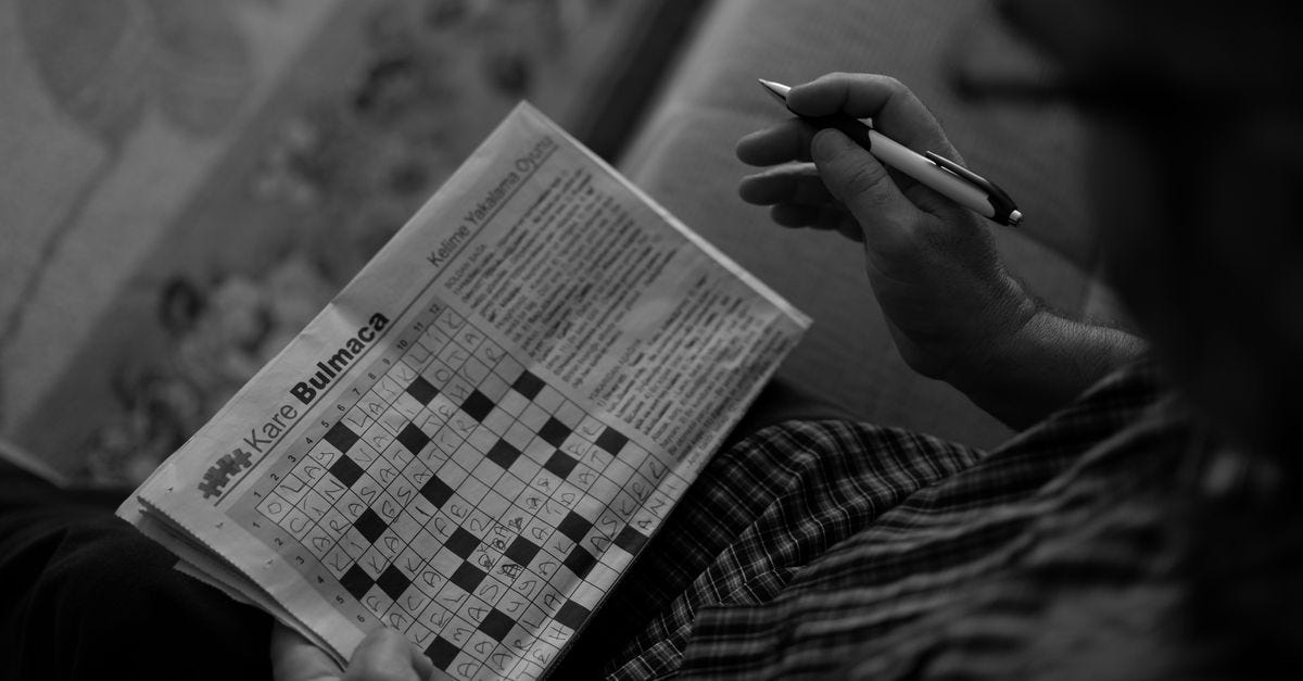A person solving a monochrome crossword puzzle indoors, using a pen.
