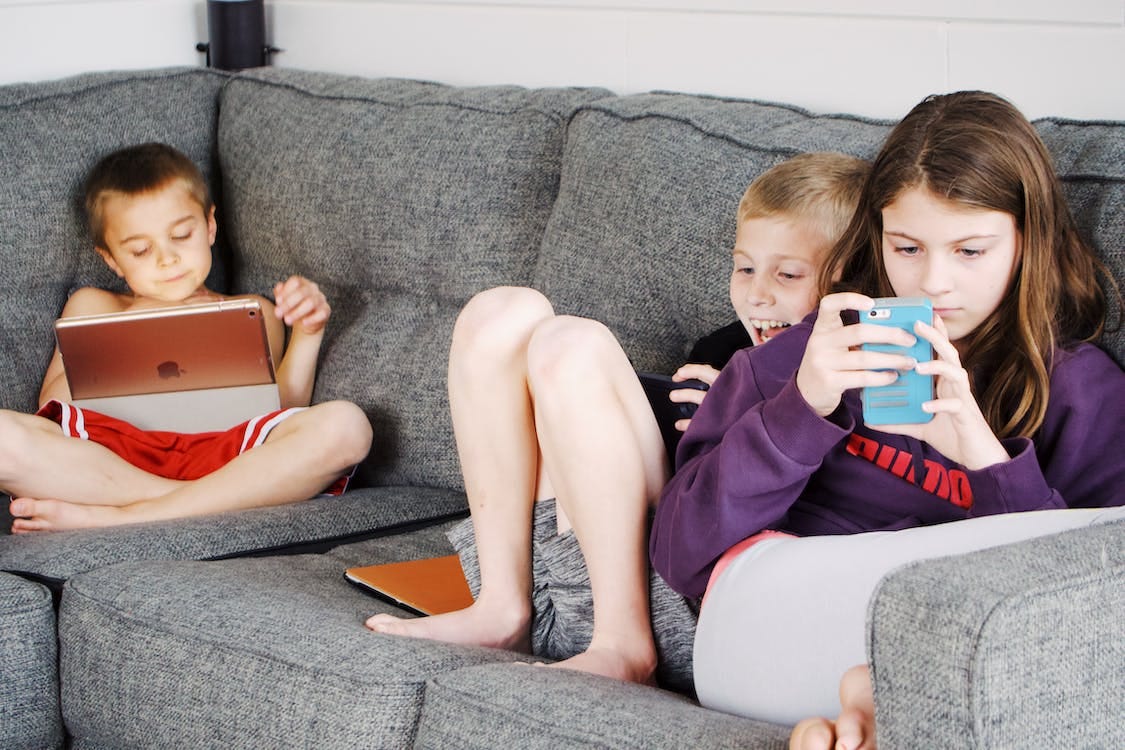 Free Positive barefoot children in casual wear resting together on cozy couch and browsing tablets and smartphones Stock Photo Free Positive barefoot children in casual wear resting together on cozy couch and browsing tablets and smartphones Stock Photo